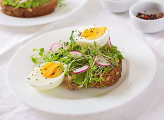 Healthy food. Breakfast. Avocado egg sandwich with whole grain bread on white wooden background.