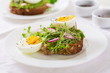 Healthy food. Breakfast. Avocado egg sandwich with whole grain bread on white wooden background.