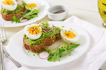 Healthy food. Breakfast. Avocado egg sandwich with whole grain bread on white wooden background.