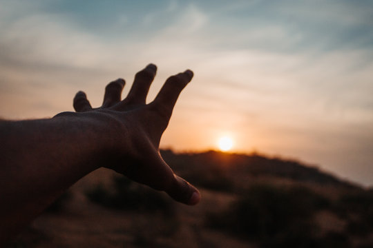 Hand reaching out to sun during sunset