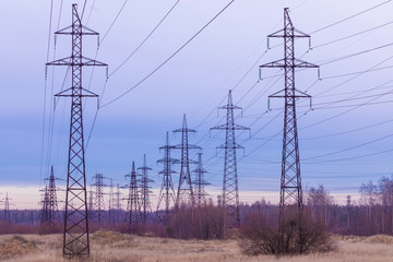 The towers of electric main in the countryside field on the background of blue sky and the forest with the wires