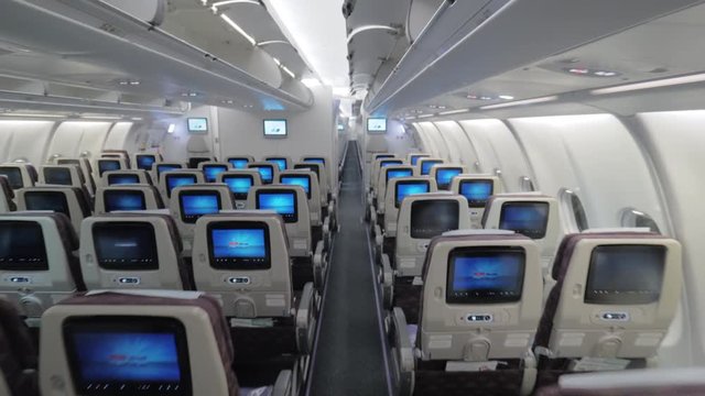 Wide shot of a jet airplane interior view without people seated inside the cabin, back of the seats with tv-monitors are visible
