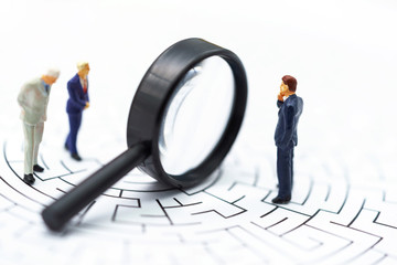 .Miniature people: Businessman use magnifying glass to find the route on the maze. Concepts of...