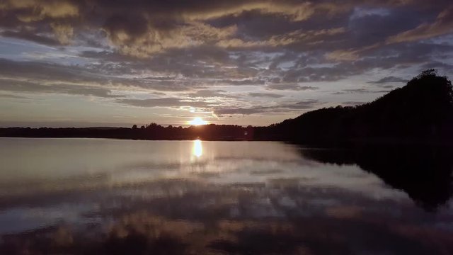 Drone flying into sunset over Scenic Swedish lake called Levrasj&radic;&part;n in Brom&radic;&part;lla during a beautiful sunset on a warm summer evening at the lake in Sk&radic;&bull;ne Sweden. Reflections of the sky in the water.