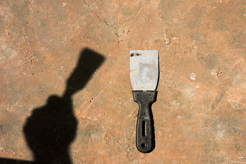 Spatula on the concrete surface and the shadow of the hand with the tool