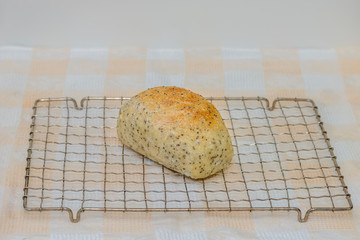 freshly baked loaf of white bread with Chia seeds on a metal grate, on a white checkered tablecloth