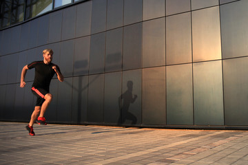 Obraz na płótnie Canvas Sporty young man running outdoors to stay healthy, at sunset or sunrise. Runner.