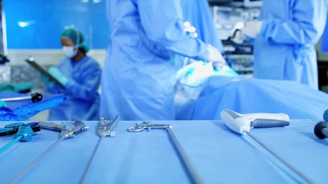 Multi ethnic healthcare surgical hospital training team in scrubs working in indoor theater facility preparing to perform Laparoscopy operation on patient using surgical instruments 