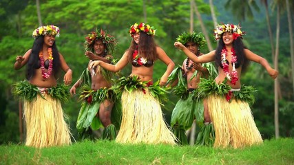 Polynesian men in warrior dress with girls in grass skirts and flower headdress dancing hula style while entertaining barefoot outdoors Tahiti French Polynesia 