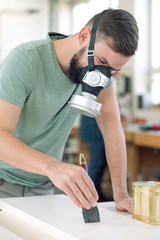 young worker in a carpenter's workshop painting wood with brush