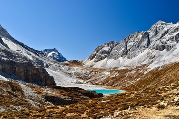 Unique colored Milk lake (approx. 4300m altitude) with blue sky and sharp mountains around it in Daocheng Yading Nature Reserve, Sichuan, China.  
