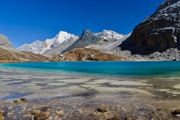 Unique colored Milk lake (approx. 4300m altitude) with blue sky and sharp mountains around it - sacred Mt. Chanadorje (Xianuoduoji,5958m) on the left. Daocheng Yading Nature Reserve, Sichuan, China.  