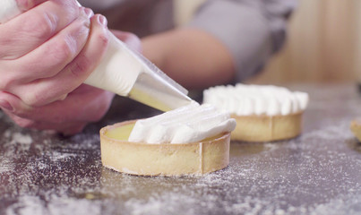 Close up hands of a confectioner decorating tartlets with swiss meringue