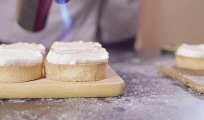 Close up hands of a confectioner burning swiss meringue on tartlets