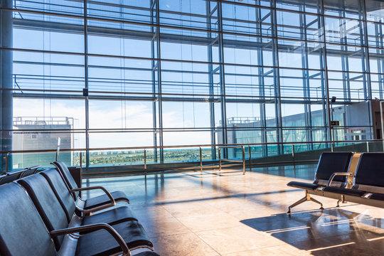 Airport empty lounge waiting area with no people. Rows of chairs big windows with view onto landing field. Sunlight streaming through glass wall. Conceptual atmospheric image