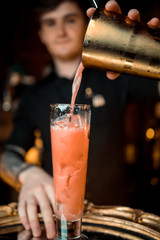 The barman pours alcohol into a glass. Close-up.