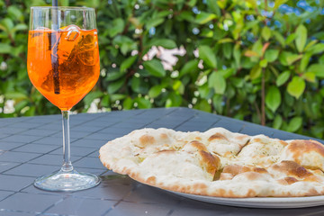Wine glass of Aperol Spritz beside some Italian garlic pizza bread.