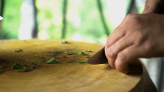Healthy green uncooked vegetables being chopped on wooden chopping board with knife in Balinese kitchen