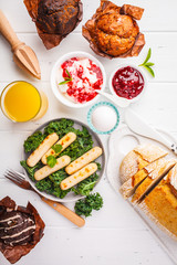 Breakfast served with muffins, grilled sausages, juice, fresh bread and parfait on white wooden table.