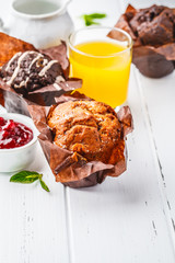 Different types of muffins on white table with juice and milk for breakfast.