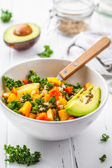 Vegan salad with rice, kale, baked pumpkin, carrots and avocado in white bowl on white wooden background.