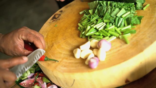 Chef in class kitchen chopping selection of healthy raw vegetables with knife on wooden cutting board