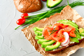 sandwich with avocado and salmon on a light background, green onions and gluten-free grain bread, radishes and tomatoes. concept diet food, copy space, sandwich take away, healthy fast food