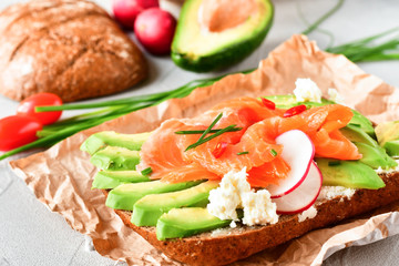 Fototapeta na wymiar sandwich with avocado and salmon on a light background, green onions and gluten-free grain bread, radishes and tomatoes. concept diet food, copy space, sandwich take away, healthy fast food
