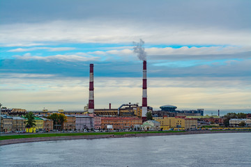 Factory chimney with smoke in the city by the river