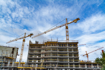Construction crane at a construction site with an unfinished house against the blue sky and clouds