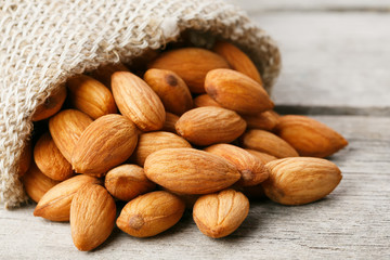 Almond nuts in a burlap bag on a wooden gray background.