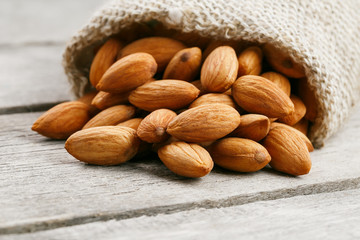 Almond nuts in a burlap bag on a wooden gray background.