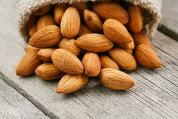 Almond nuts in a burlap bag on a wooden gray background.