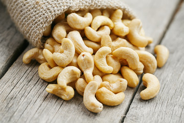 Cashew nuts in burlap bag on wooden gray background . Healthy food