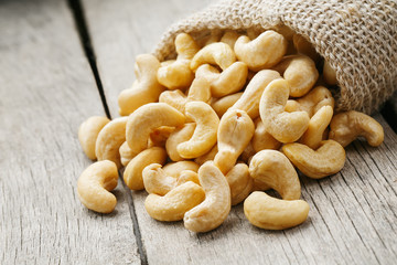 Cashew nuts in burlap bag on wooden gray background . Healthy food