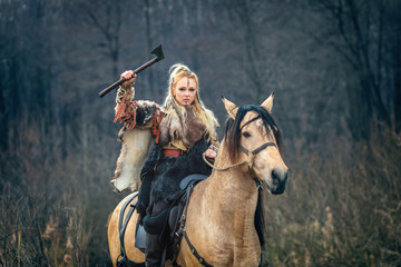 Scandinavian viking woman warrior riding horse holding ax above head looking threateningly....