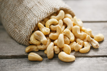 Cashew nuts in burlap bag on wooden gray background . Healthy food