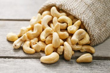 Cashew nuts in burlap bag on wooden gray background . Healthy food