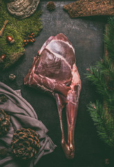 Raw aged leg of venison with bone on dark kitchen table background , top view. Raw meat leg of deer. Cooking preparation of venison roast - obrazy, fototapety, plakaty