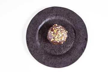Rum ball decorated with chocolate and nuts on a black plate on a white background