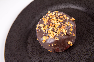 Rum ball decorated with chocolate and nuts on a black plate on a white background