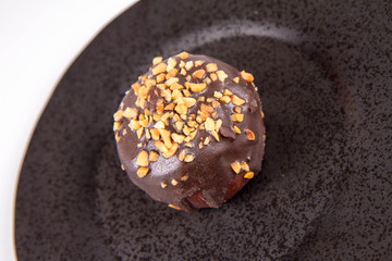 Rum ball decorated with chocolate and nuts on a black plate on a white background