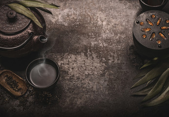 Dark asian tea background with black iron teapot and mug of green tea. Copy space for your design....