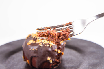 Rum ball decorated with chocolate and nuts on a black plate, partially eaten, on a white background