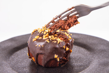 Rum ball decorated with chocolate and nuts on a black plate, partially eaten, on a white background