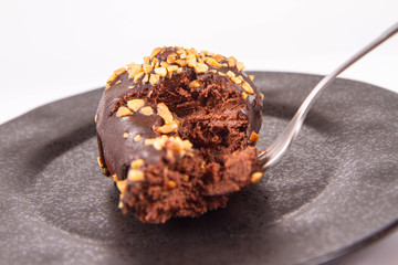 Rum ball decorated with chocolate and nuts on a black plate, partially eaten, on a white background