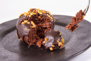 Rum ball decorated with chocolate and nuts on a black plate, partially eaten, on a white background