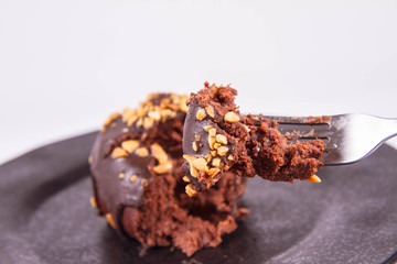 Rum ball decorated with chocolate and nuts on a black plate, partially eaten, on a white background
