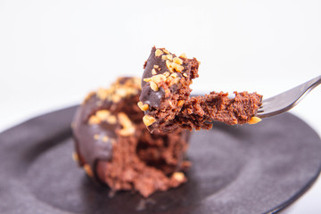 Rum ball decorated with chocolate and nuts on a black plate eaten with a fork on a white background