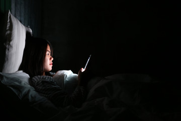 Asian woman using smartphone for checking social media with icon or hologram at night on the bed in...